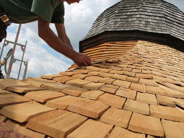 Hand legt Holzschindeln auf eine runde Dachfläche
