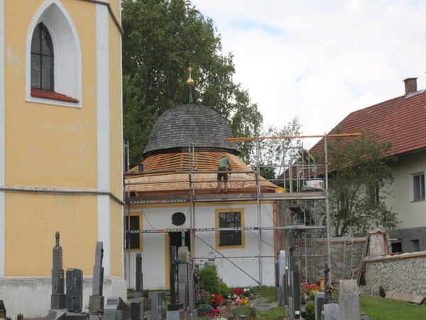 Kapelle mit eingerüstetem Schindeldach neben einer Kirche